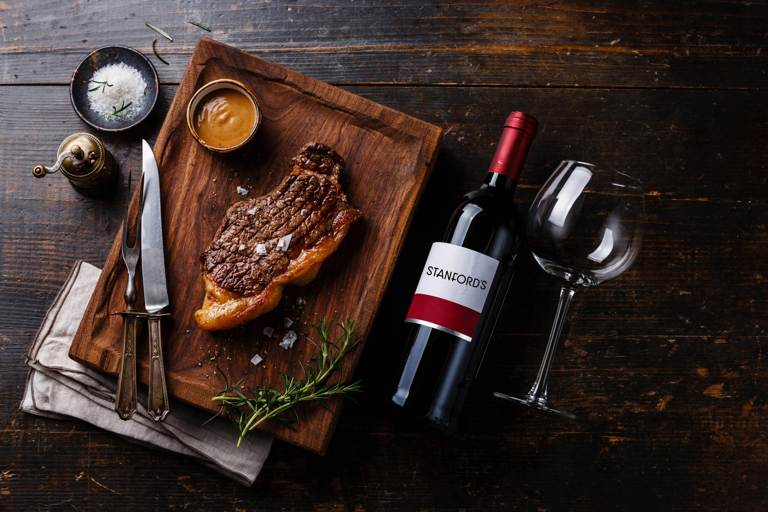 Grilled Steak Striploin with Pepper sauce and bottle of Red wine on wooden background